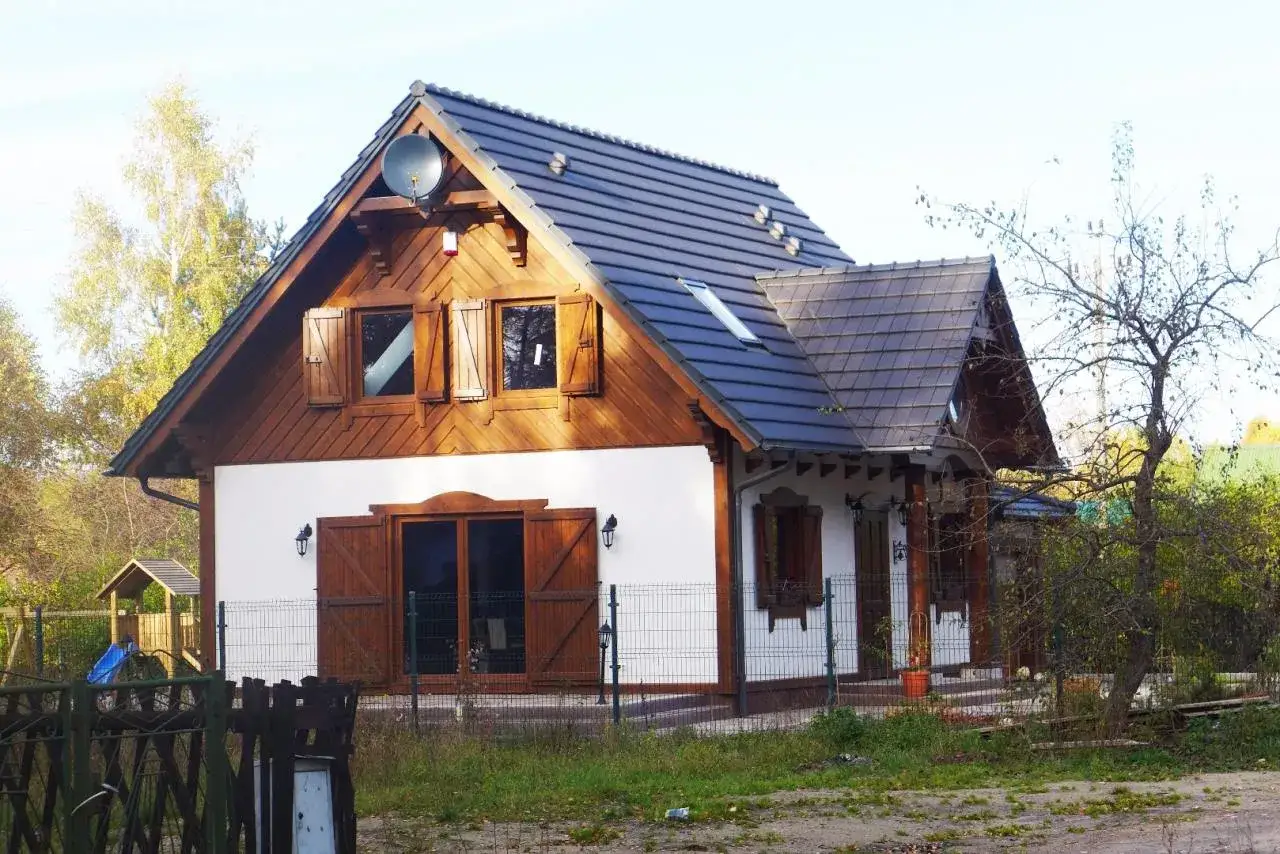 Nowoczesne domy w stylu dworkowym z drewnianymi elementami i białymi ścianami, otoczone zielenią.