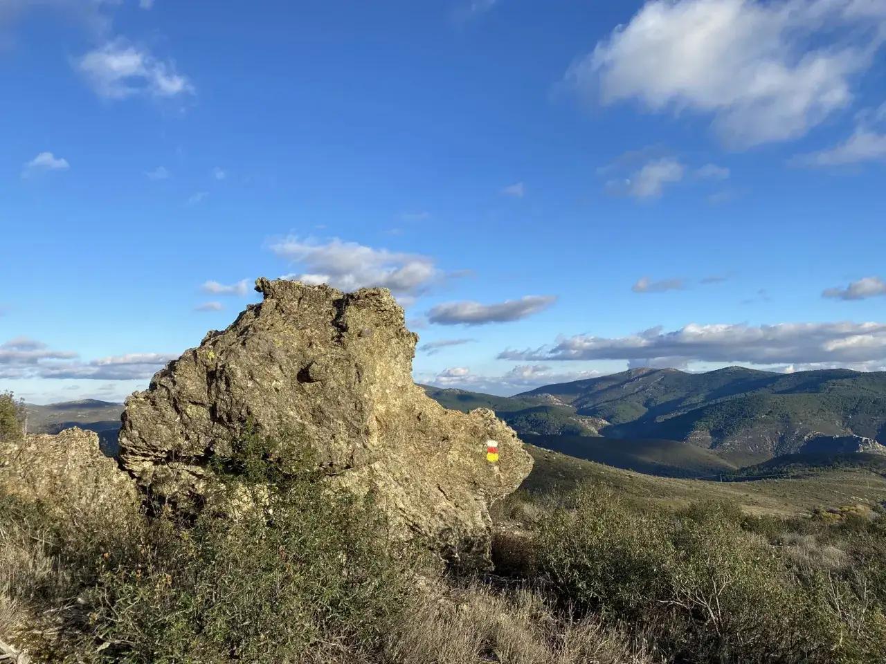 Roca con marcas de sendero, inicio de un arbancon paseo magico. Paisaje monta&ntilde;oso y cielo azul con nubes.