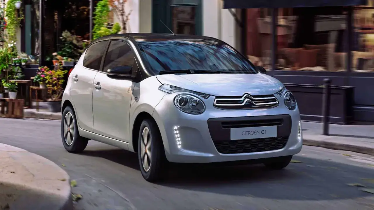 Biały Citroen C1 z czarnym dachem jedzie ulicą.