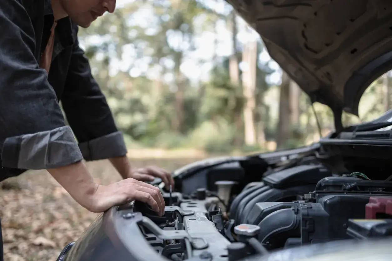 Un homme regarde le moteur de sa voiture qui cale à bas régime, bloqué en pleine nature.