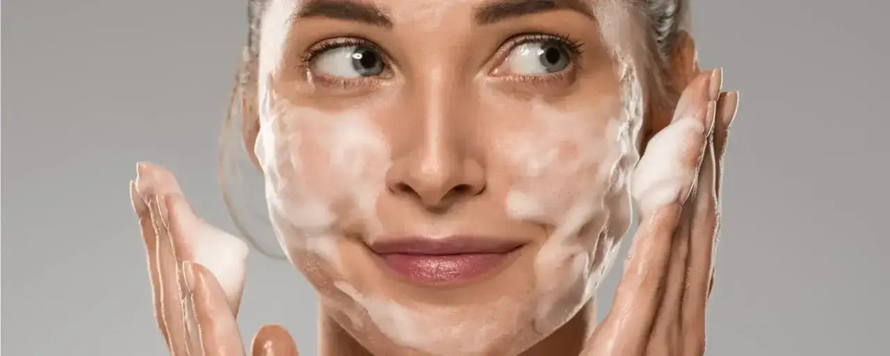 Donna con schiuma sul viso, mentre si lava. La scelta è tra prima scrub o detergente per una pelle luminosa.
