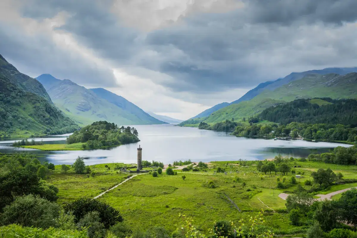 A dramatic Scottish landscape with a monument on a grassy knoll overlooking a vast loch, perfect for a scotland hiking itinerary.
