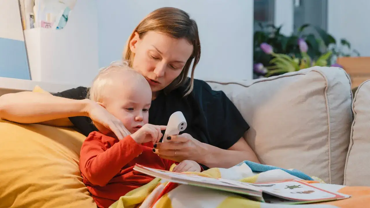 Als alleinerziehende Mutter k&uuml;mmere ich mich um mein krankes Kind. Wir lesen ein Buch, w&auml;hrend ich seine Temperatur messe.