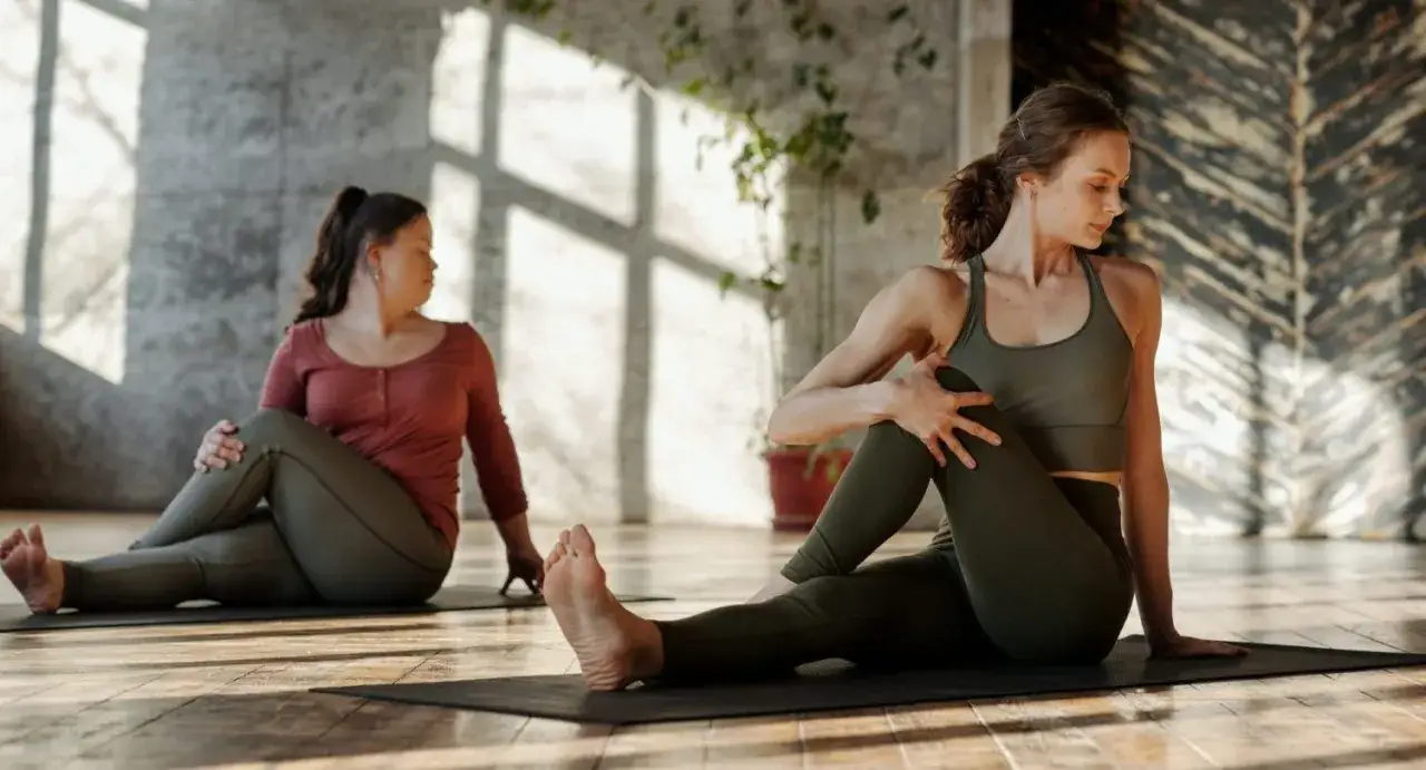 Dos mujeres realizan una torsi&oacute;n sentada, un ejercicio ideal para aprender c&oacute;mo estirar la espalda baja y mejorar la flexibilidad.