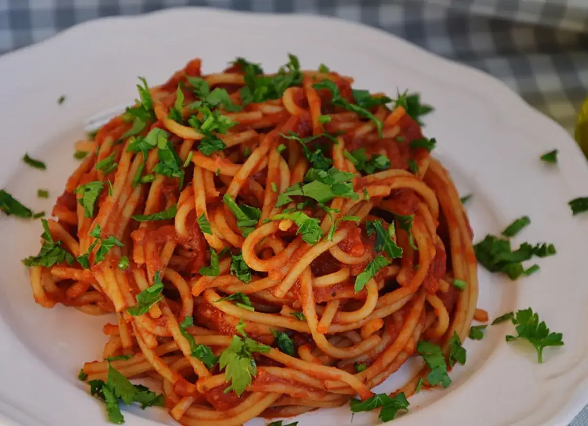 Porcja spaghetti z sosem pomidorowym i posiekaną natką pietruszki, gotowa do posypania ulubionym serem do spaghetti.