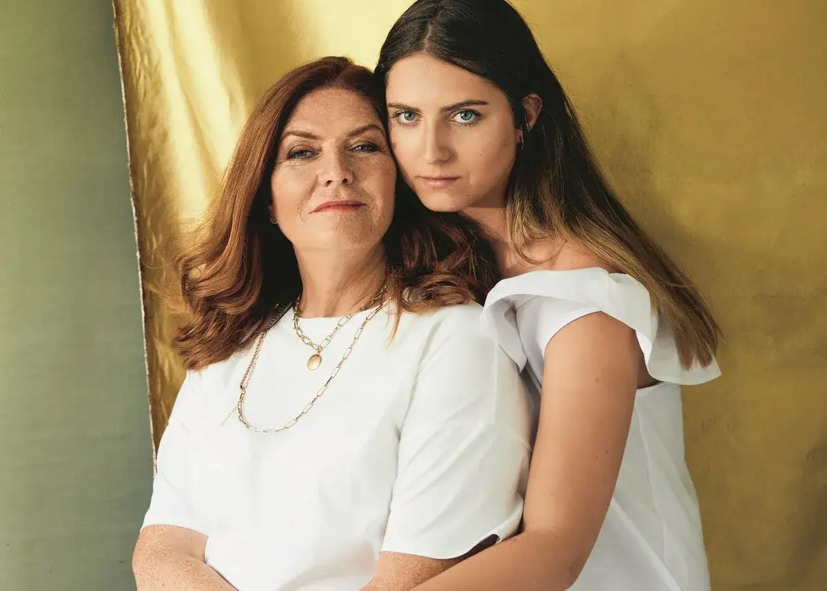 Maria Dowbor Baczyńska i jej córka, obie w białych bluzkach, przytulają się na tle złotej tkaniny.