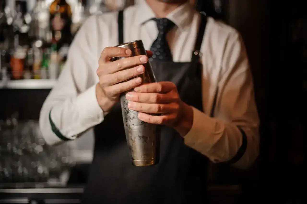 Barman w fartuchu miesza drinki w metalowym shakerze do drinków.