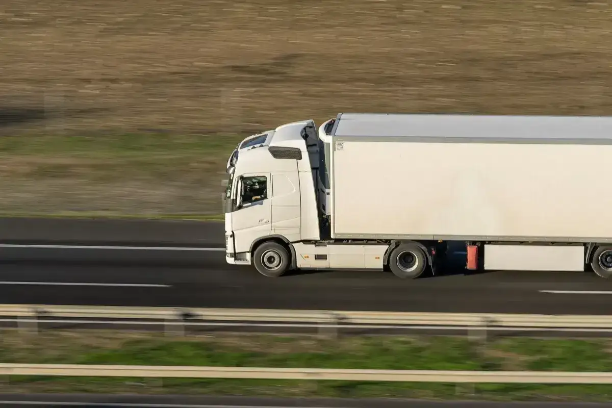 Biała ciężarówka z naczepą jedzie autostradą. Usługa kierowania pojazdem powierzonym PKD w ruchu.