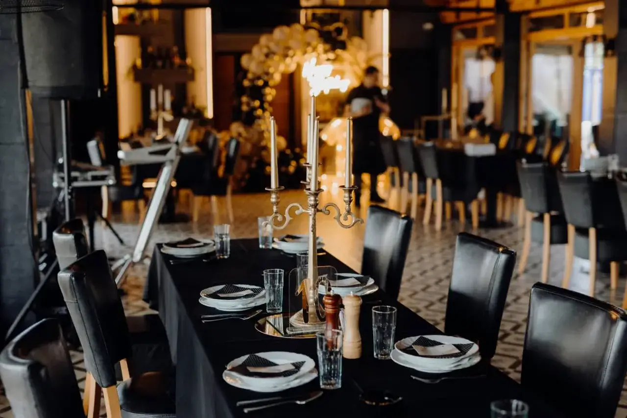 Ett l&aring;ngt matbord f&ouml;r 12 personer &auml;r dukat med svarta dukar, ljusstakar och glas. Stolar i l&auml;der omger bordet i en elegant restaurangmilj&ouml;.