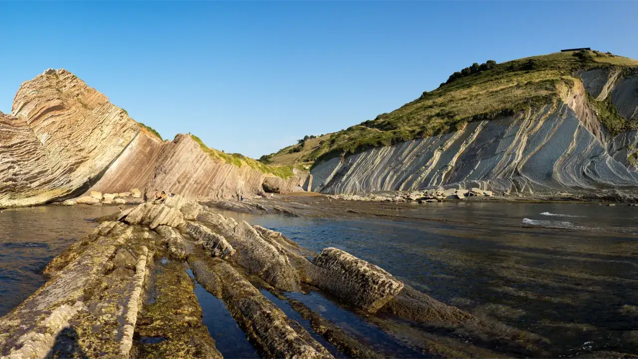 El camí de ronda l'Escala revela formaciones rocosas estratificadas y el mar azul bajo un cielo despejado.