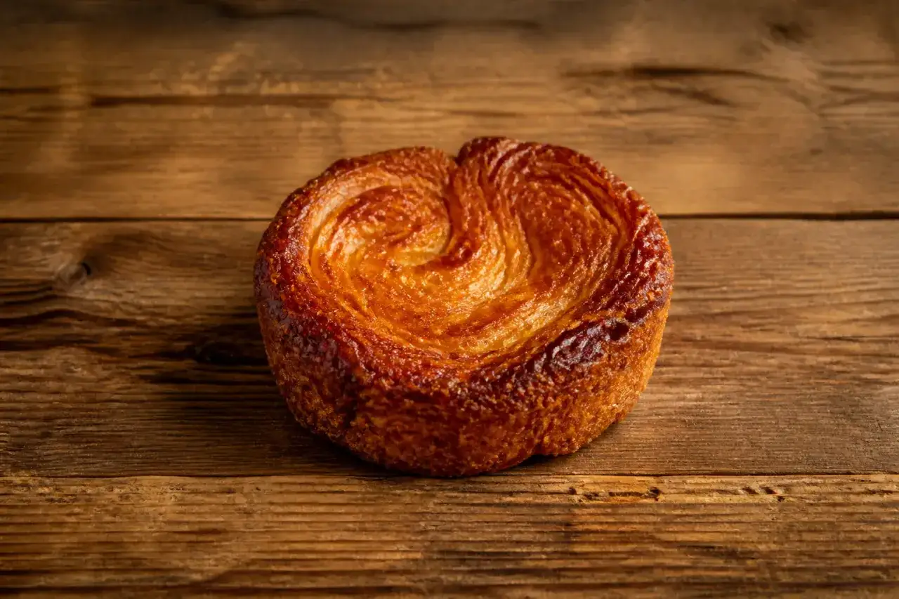 Une d&eacute;licieuse composition de kouign amann, dor&eacute; et feuillet&eacute;, pos&eacute; sur un fond de bois rustique.