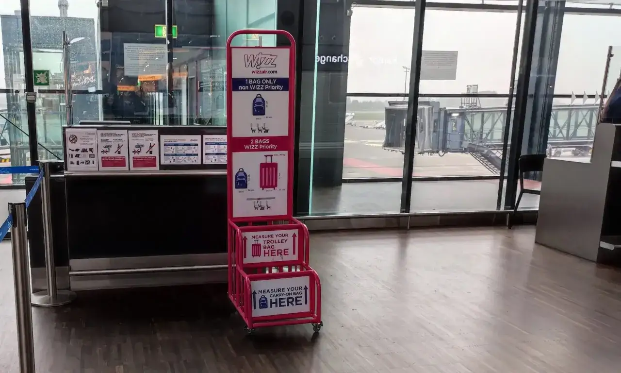 Różowy stojak Wizzair z miarkami do bagażu podręcznego na lotnisku.