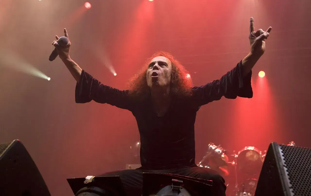 Ronnie James Dio zespół na scenie, z rękami w górze i mikrofonem. Czerwone światła tworzą mistyczną atmosferę.