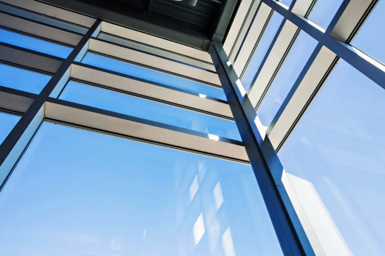 Ventana moderna con cristales polarizados que reflejan el cielo azul y la estructura del edificio.