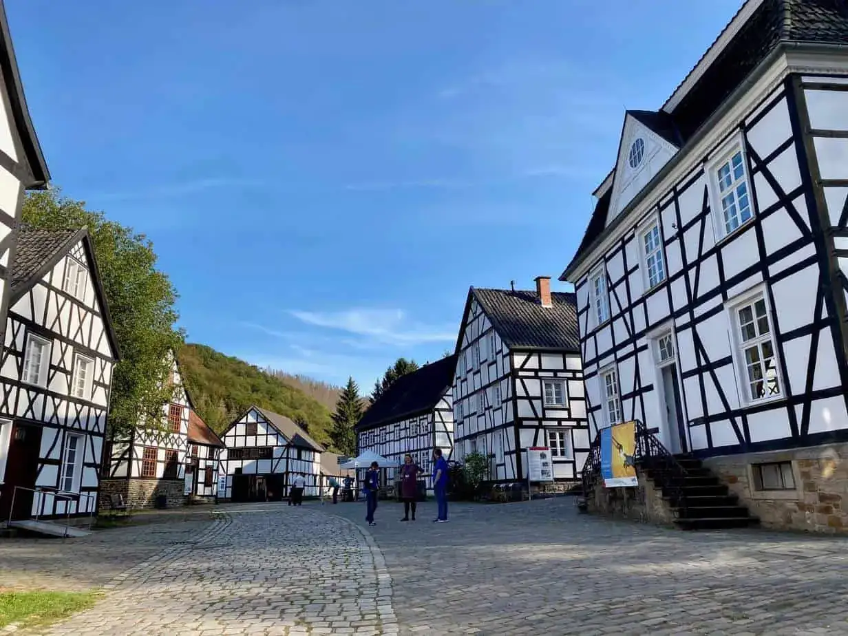 Fachwerkhäuser in einem Dorf, das zeigt, was ein Freilichtmuseum ist. Besucher schlendern über Kopfsteinpflaster unter blauem Himmel.