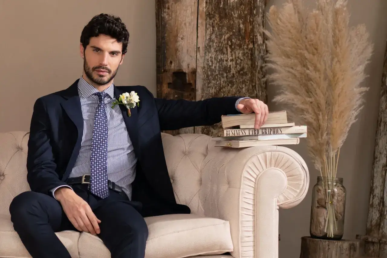 Uomo elegante con camicia a righe, giacca blu e cravatta, che sfoglia libri. L'arte della camicia &egrave; evidente nel suo stile impeccabile.