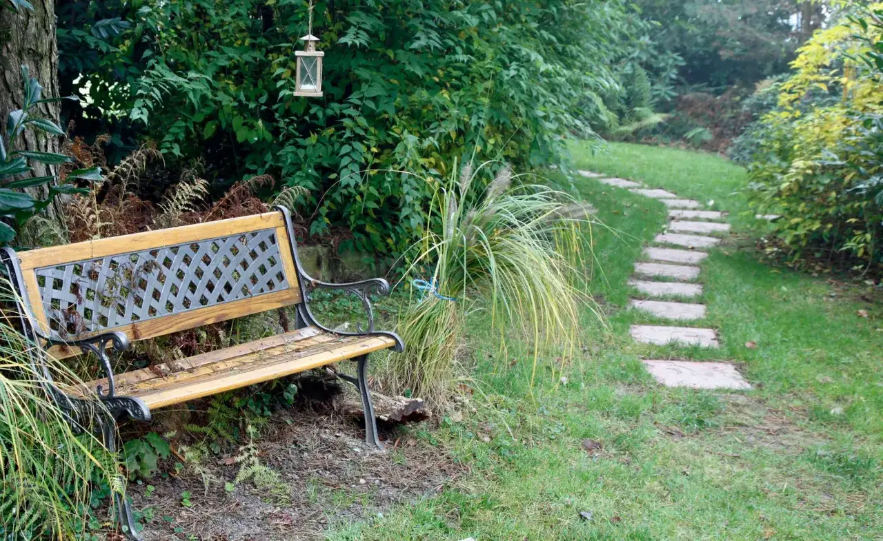 Ein rustiger **Bauerngarten** mit einem Holzbank und Steinplatten-**Wege**, die sich durch üppiges Grün schlängeln. Eine Laterne hängt im Baum.