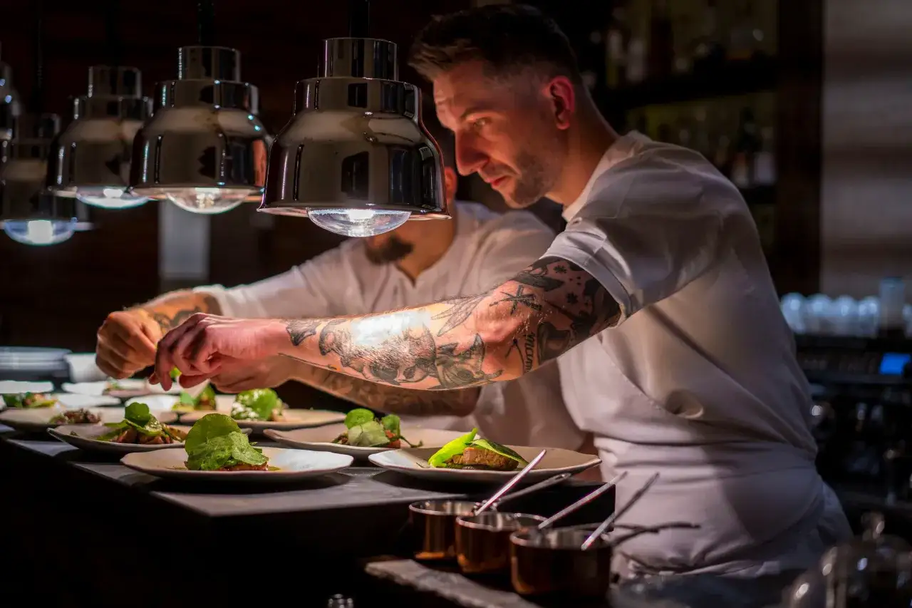 Szef kuchni z tatuażami dopracowuje dania w jednej z najlepszych restauracji z gwiazdką michelin polska.