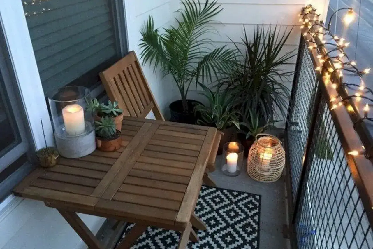 Przytulny balkon inspiracje: drewniany stolik, krzesło, rośliny, świece i girlanda świetlna tworzą magiczny nastrój.