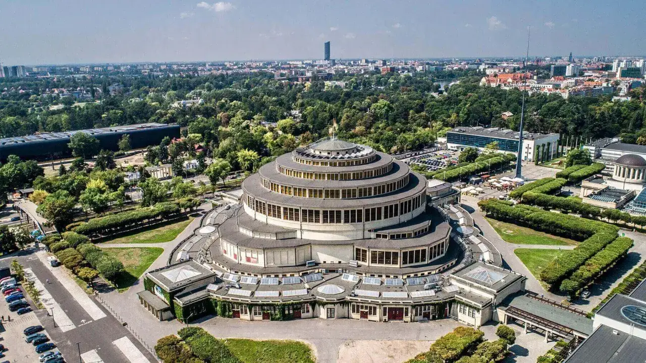 Die Jahrhunderthalle Breslau, ein beeindruckendes kreisf&ouml;rmiges Geb&auml;ude, ragt inmitten einer gr&uuml;nen Parkanlage und der Stadtkulisse empor.