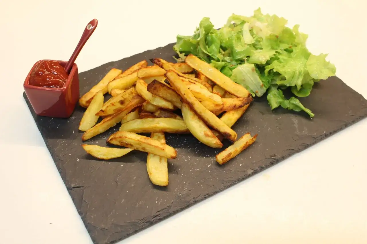 Une assiette de frites au four dorées, accompagnées d'une salade verte et d'une coupelle de ketchup.