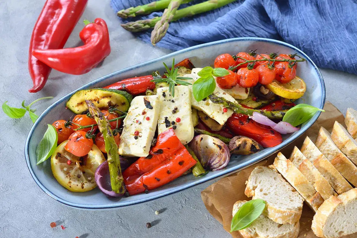 Bunter, gegrillter Gem&uuml;se-Feta-Salat mit Kirschtomaten, Zucchini, Paprika und Spargel, garniert mit Basilikum und Rosmarin. Dazu Baguettescheiben.