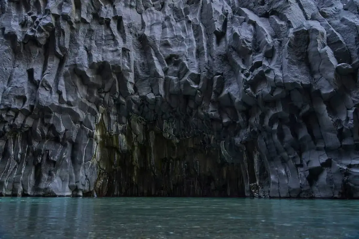 Die Alcantara Schlucht in Sizilien zeigt beeindruckende Basalts&auml;ulen, die vom Fluss geformt wurden. Das klare Wasser spiegelt die dunklen Felsw&auml;nde wider.
