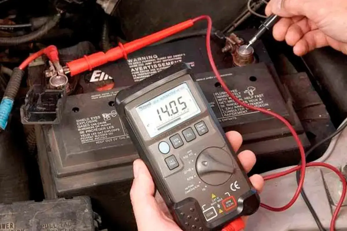 A person uses a multimeter to test a car battery, displaying 14.05 volts. This is a step in how to test alternator function.