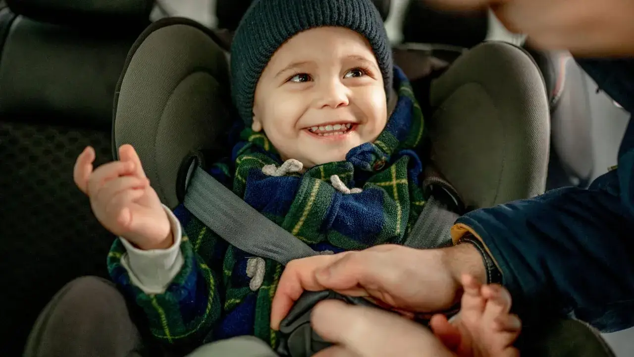 Ein l&auml;chelndes Kind im Kindersitz, bereit f&uuml;r die Fahrt. Die Frage 