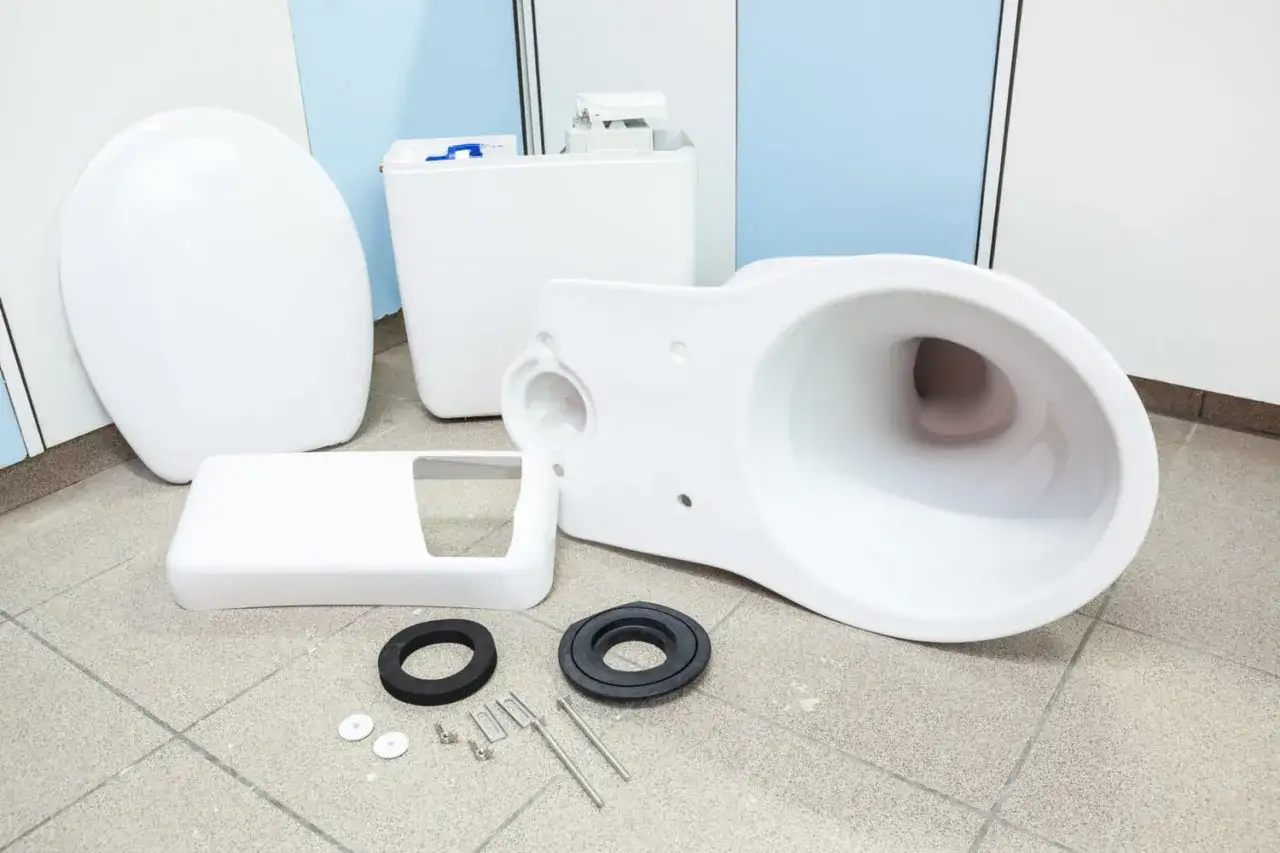 Pi&egrave;ces d'un nouveau WC blanc d&eacute;mont&eacute;es sur le sol, pr&ecirc;tes pour le sch&eacute;ma d'installation.