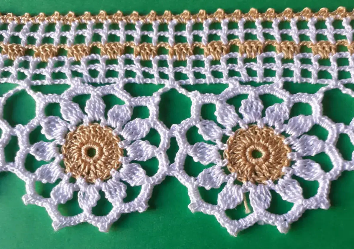 Bordo di **merletti uncinetto** bianchi e dorati, con motivi floreali e geometrici, su sfondo verde.