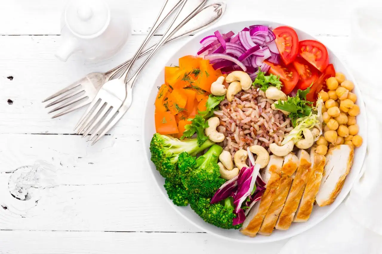 Kolorowa miska z ryżem, kurczakiem, brokułami, dynią, ciecierzycą i orzechami nerkowca. Zdrowe obiady na wysoki cholesterol.