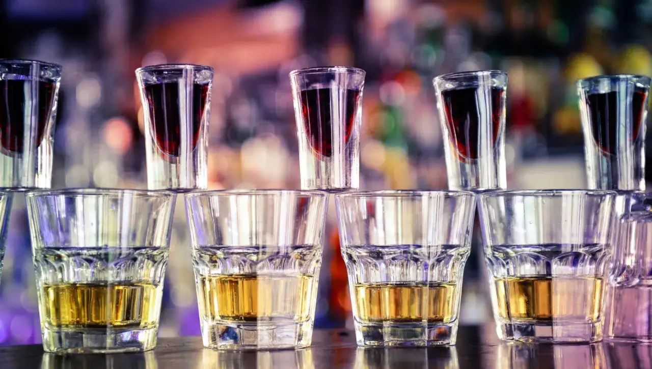 Szklanki z bursztynowym płynem i shoty z ciemnym drinkiem z jagermeister.