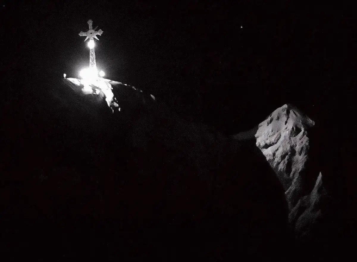 Nocna panorama Tatr. Jasno oświetlony krzyż na Giewoncie góruje nad ciemnymi szczytami. Czy krzyż na Giewoncie świeci? Tak, jego światło rozświetla noc.