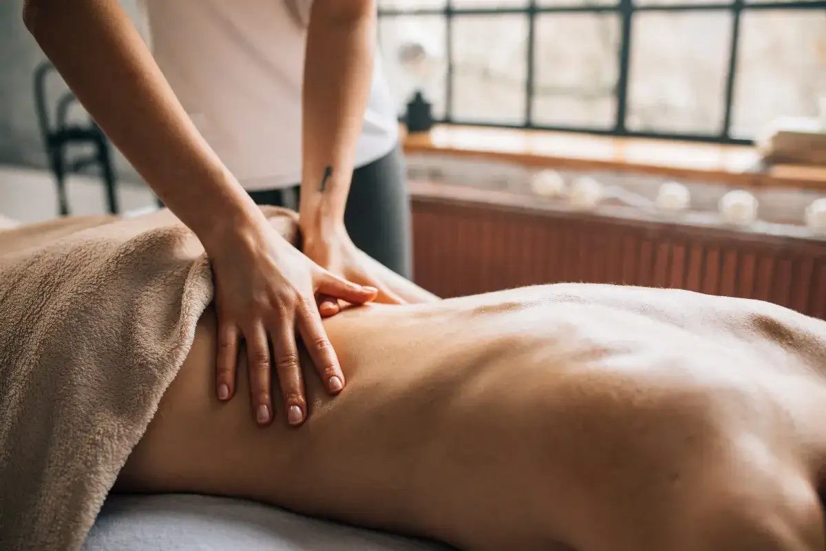 Dłonie terapeuty wykonują relaksujący masaż ajurwedyjski na plecach klienta, otulonego miękkim ręcznikiem.