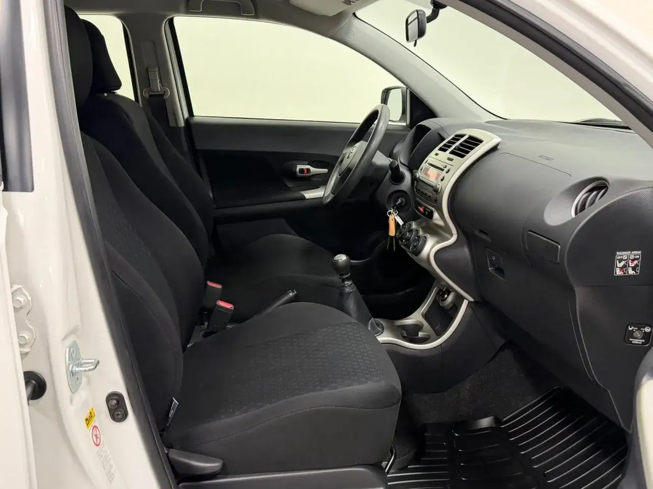 Interiörbild på en Toyota Urban Cruiser. Framstolarna är svarta och tygklädda. Instrumentpanelen är mörkgrå med silverdetaljer. En växellåda och en ratt syns. Inga uppenbara problem med denna Toyota Urban Cruiser.
