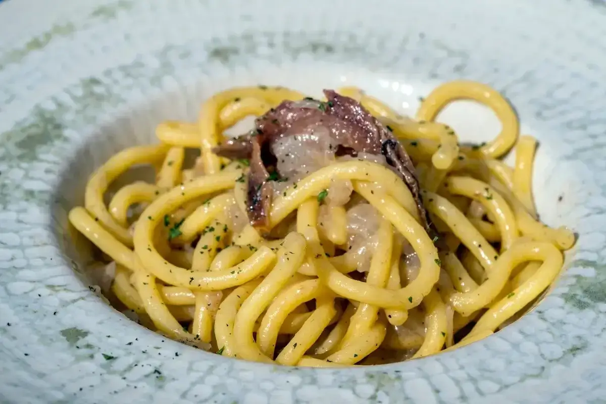 Un piatto di bigoli in salsa, pasta spessa condita con acciughe e cipolla, guarnita con prezzemolo tritato.