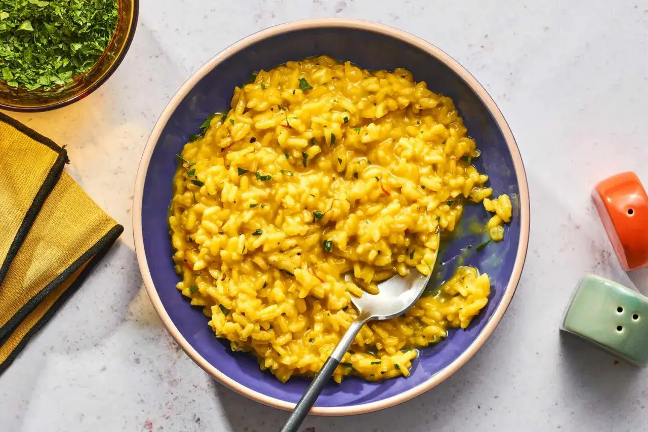 Un cremoso risotto a la milanesa, con hebras de azafr&aacute;n y perejil picado, servido en un cuenco morado.