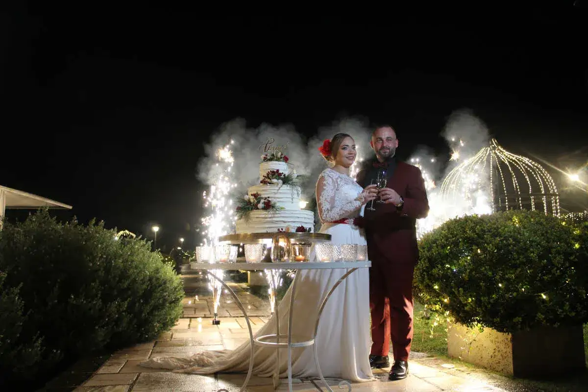Sposi brindano con fuochi d'artificio per matrimonio, una torta nuziale illuminata da scintille.