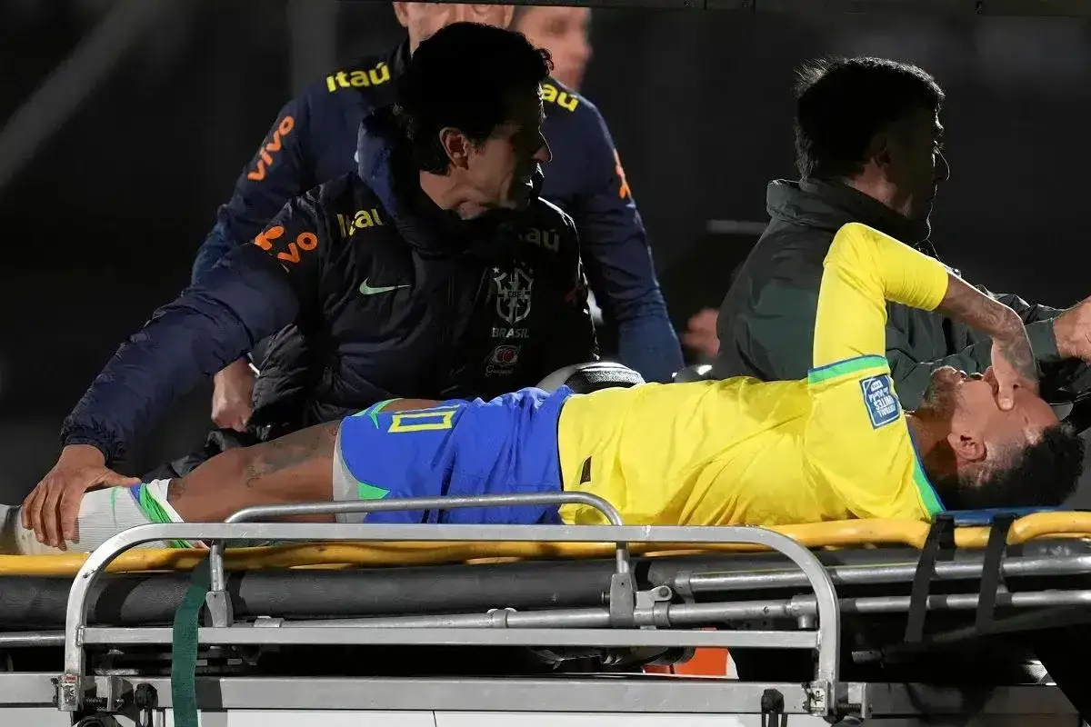 Neymar leży na noszach, z bólu zakrywając twarz. Jego kontuzja wygląda poważnie, a sztab medyczny otacza go troską.