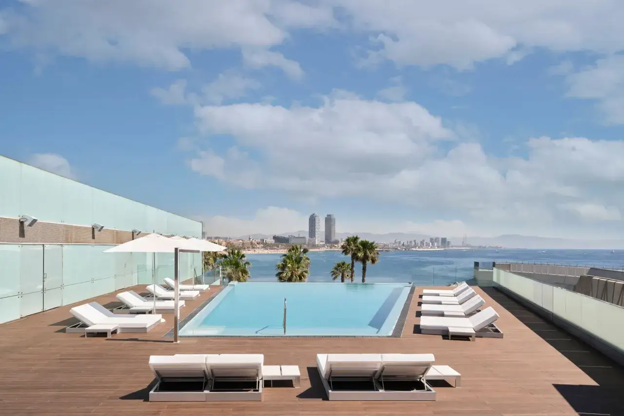 Piscina a sfioro su un w barcelona rooftop bar, con vista sul mare e sullo skyline della città. Lettini bianchi e palme creano un'atmosfera rilassante.