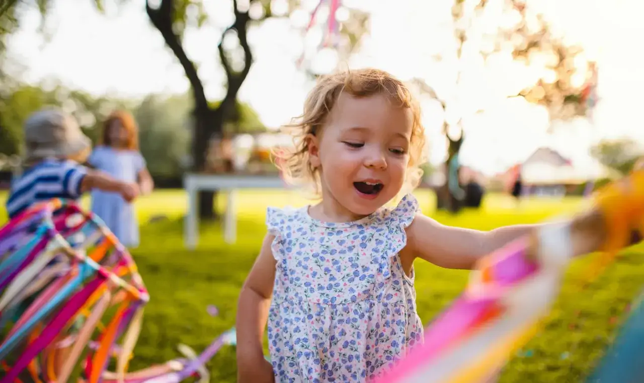 Ein fröhliches kleines Mädchen mit blonden Locken spielt im Garten. Bald muss ein Kind in den Kindergarten, aber jetzt genießt es die bunte Deko.