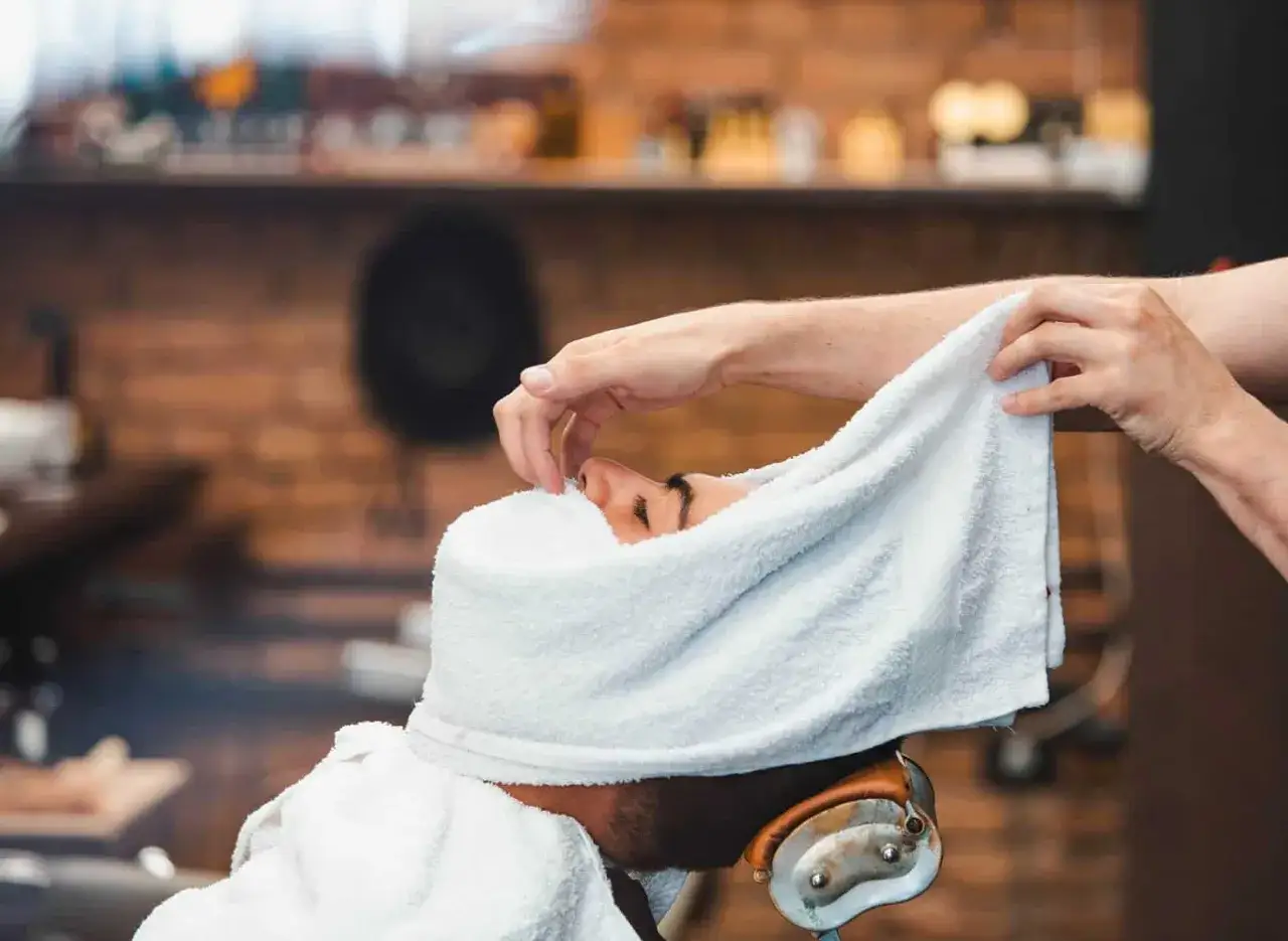 Un homme reçoit un soin du visage avec une serviette chaude. Apprenez comment faire une serviette chaude pour les cheveux pour un moment de détente.