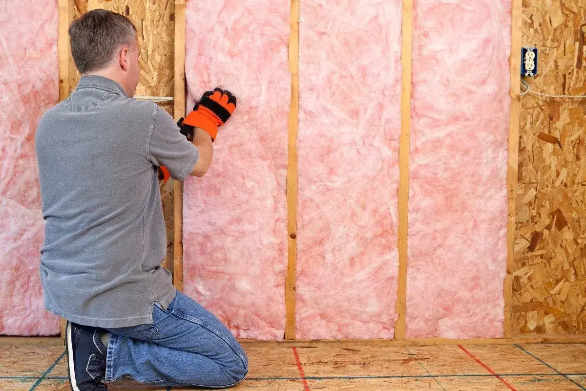 Uomo con guanti installa isolamento rosa in una parete, un passo fondamentale per l'efficientamento energetico significato.