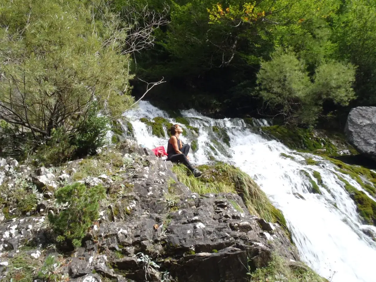 Mujer sentada en roca junto a cascada en la ruta garganta de Escuain.