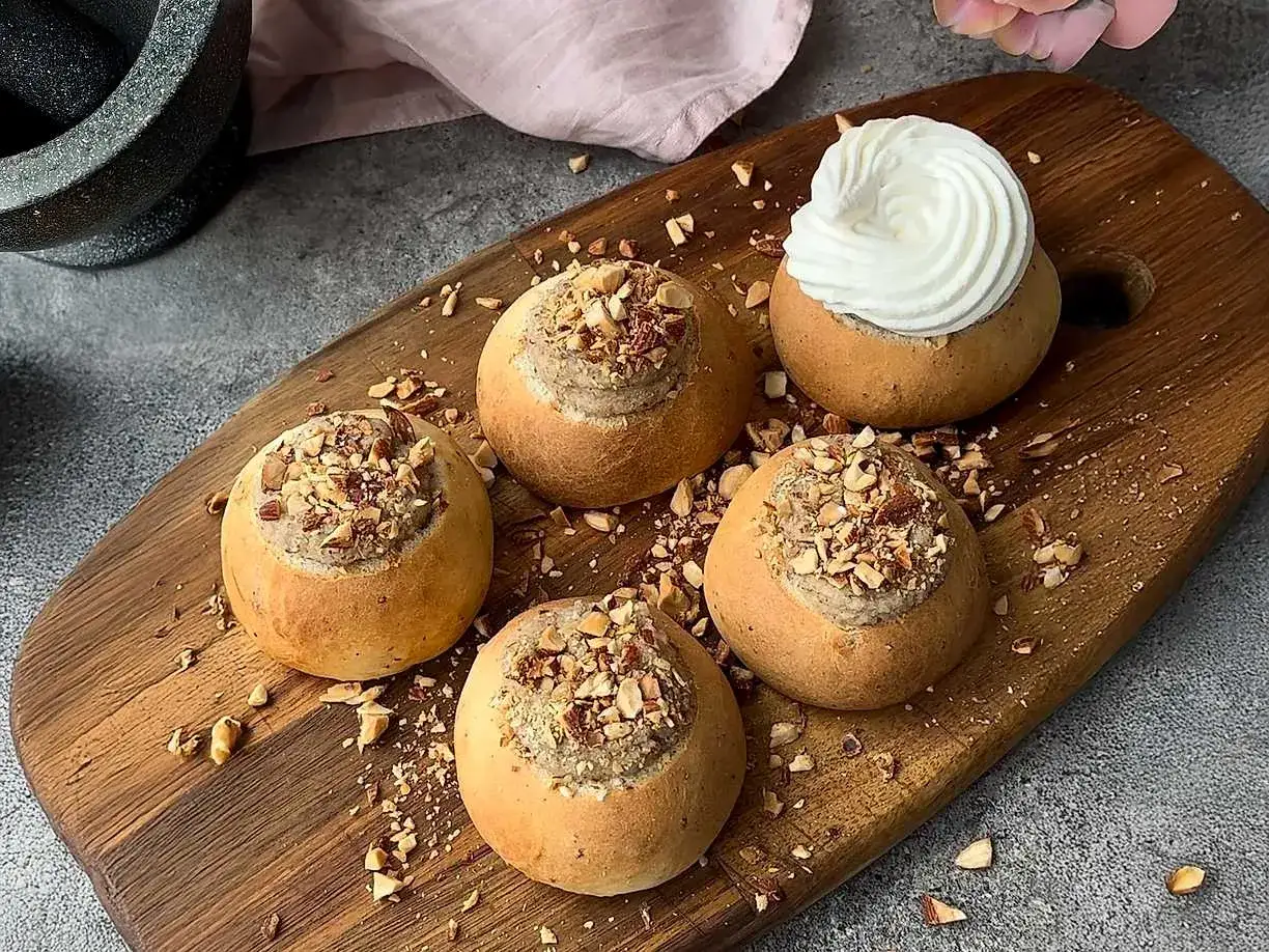 Fem nybakade semlor p&aring; ett tr&auml;fat, fyllda med h&auml;rlig mandelmassa till semlor och toppade med hackade n&ouml;tter. En &auml;r dekorerad med vispgr&auml;dde.