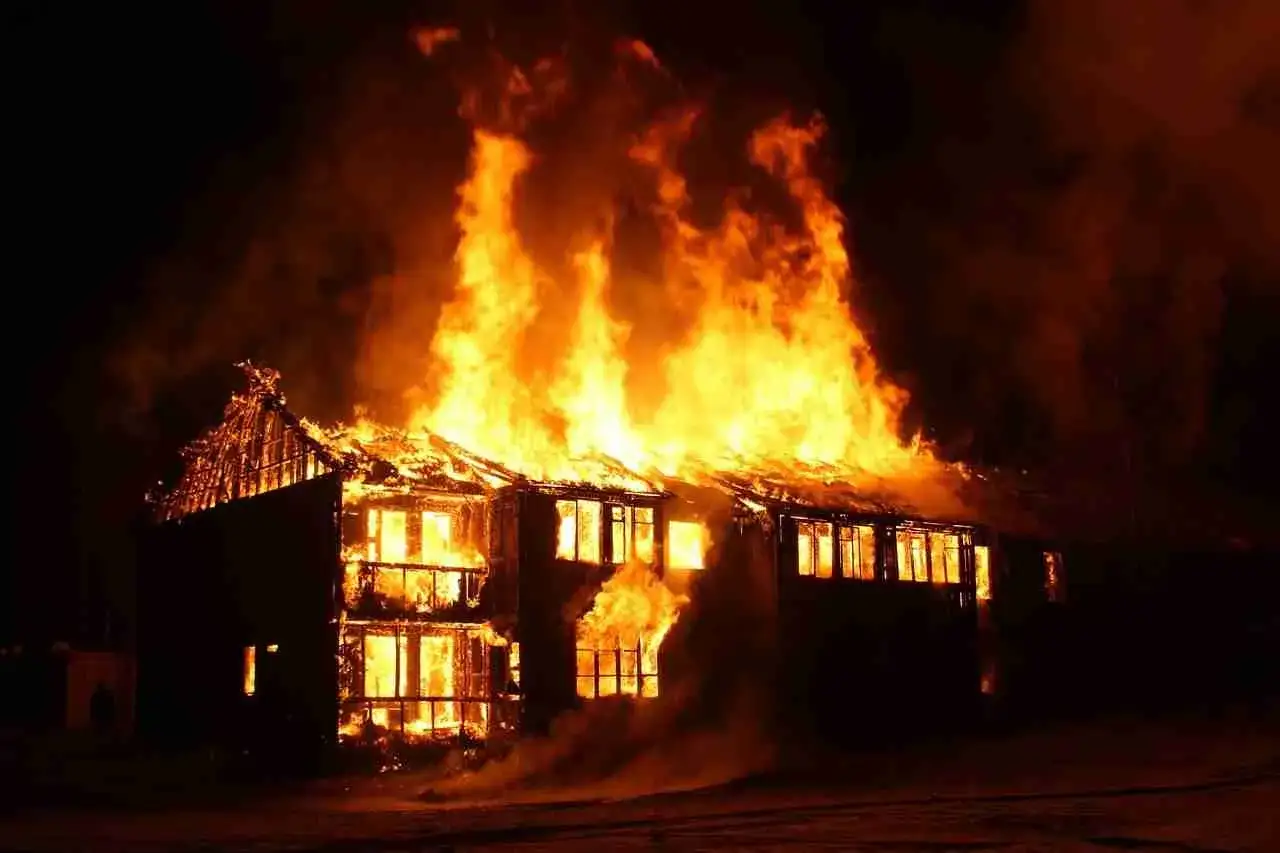 Un **incendie maison** dévaste une bâtisse de deux étages dans la nuit. Les flammes jaillissent du toit et des fenêtres, illuminant le ciel sombre.
