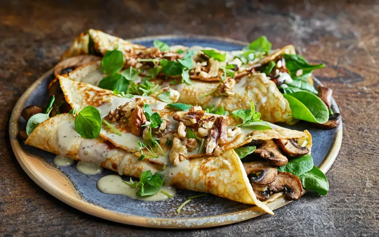 Herzhafte Pfannkuchen gefüllt mit Pilzen und Spinat, übergossen mit cremiger Sauce und garniert mit Walnüssen und frischen Kräutern.