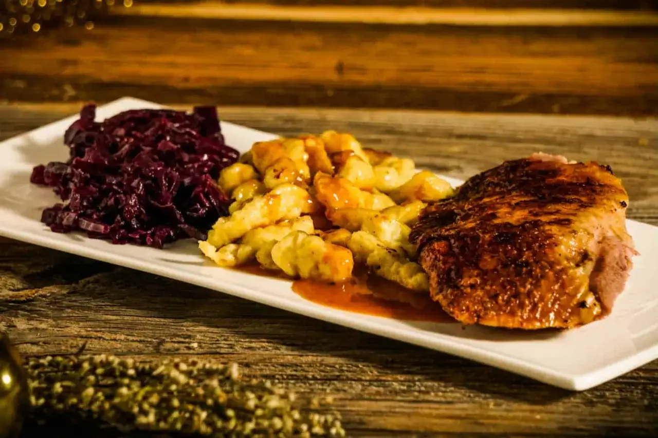 Herzhaftes Gericht mit gebratener Diepholzer Gans, Kl&ouml;&szlig;en und Rotkohl auf einem wei&szlig;en Teller.