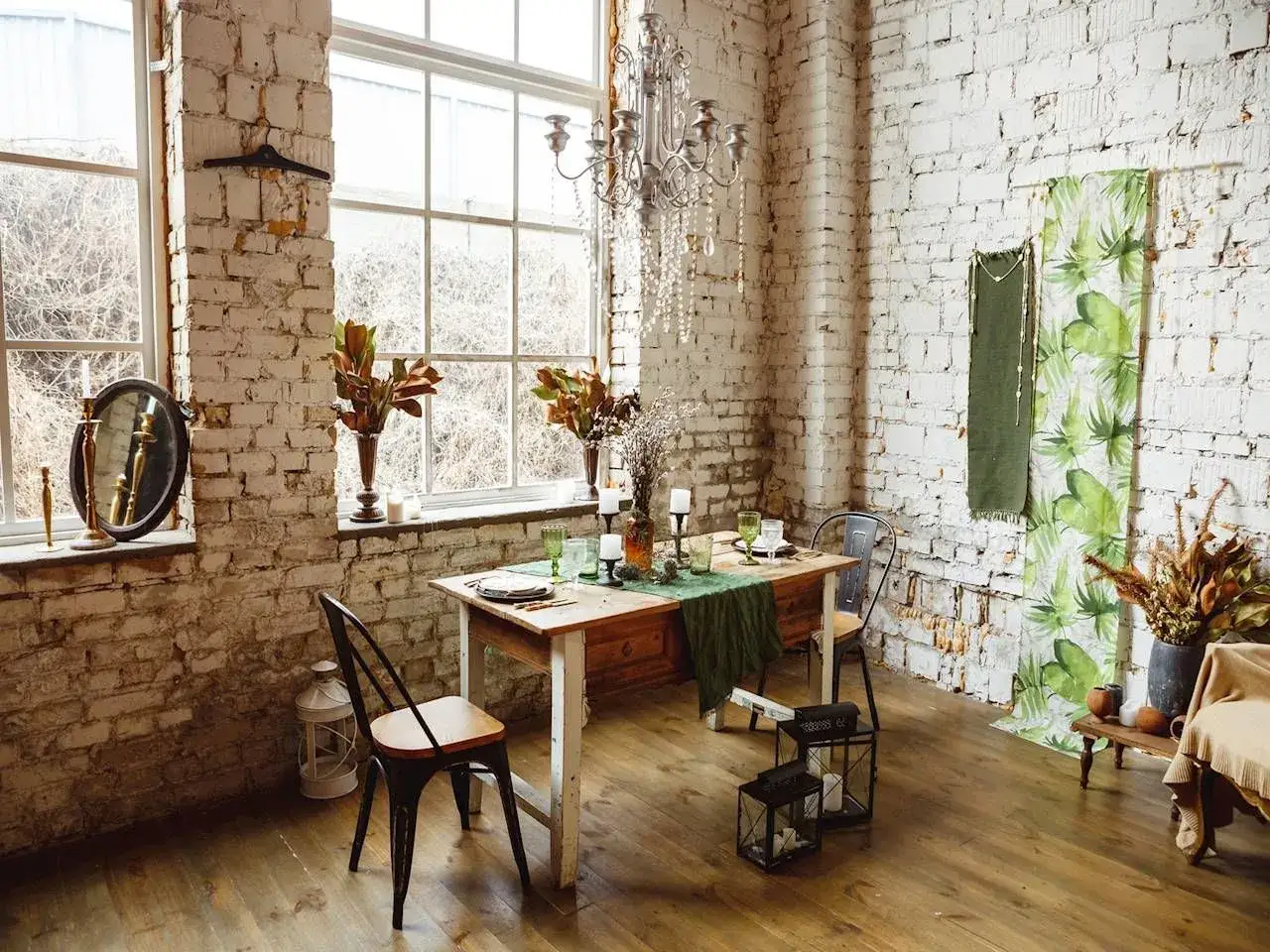 Przytulne wnętrze w stylu cottagecore: drewniany stół, ceglane ściany, świece i bukiety suszonych kwiatów tworzą sielski klimat.